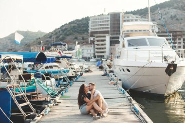 Sevgililer, erkek ve kız, ahşap bir iskelede oturuyor, el ele tutuşuyor ve gülüyorlar.