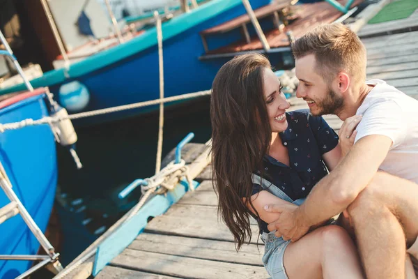 Gli amanti, ragazzo e ragazza, sono seduti su un molo di legno, tenendosi per mano e ridendo — Foto Stock