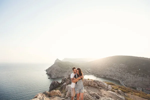 El tipo abraza a una chica en el borde de una roca de cerca sobre el fondo de una montaña. — Foto de Stock