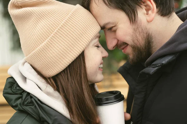 Liebevolles schönes Paar an einem Wintertag. Ein Mann umarmt seine glückliche Frau, trinkt heißen Tee oder Kaffee, während er an der frischen Luft spaziert — Stockfoto