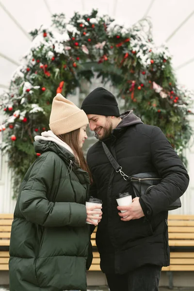 Amar belo casal em um dia de inverno. Um homem abraçando sua mulher feliz, bebendo chá quente ou café enquanto caminha ao ar livre — Fotografia de Stock