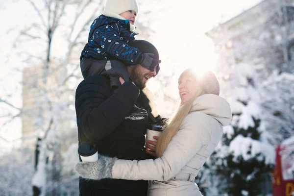 Portret van een gelukkig jong gezin dat samen wandelt in een winterpark, zonlicht. De zoon zit op papa 's nek. — Stockfoto