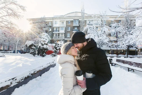 Um lindo casal amoroso em um parque de neve de inverno com café. Um homem bonito abraçando sua mulher feliz e rindo — Fotografia de Stock