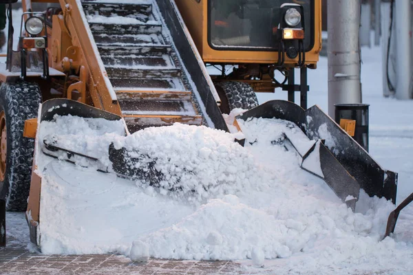 Traktor rengøring vejen fra sneen. Gravemaskine renser gaderne for store mængder sne i byen - Stock-foto
