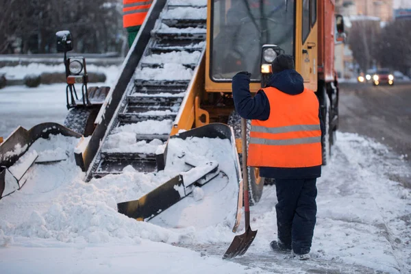 Tractor maakt de weg schoon van de sneeuw. Graafmachine reinigt de straten van grote hoeveelheden sneeuw in de stad. Werknemers vegen sneeuw van de weg in de winter, Reiniging weg van sneeuw storm — Stockfoto