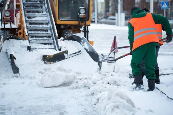 Trator limpando a estrada da neve. Escavadeira limpa as ruas de grandes quantidades de neve na cidade. Os trabalhadores varrem a neve da estrada no inverno, limpando a estrada da tempestade de neve — Fotografia de Stock