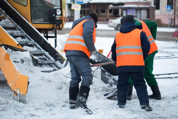 Tractor limpiando la carretera de la nieve. Excavadora limpia las calles de grandes cantidades de nieve en la ciudad. Los trabajadores barren la nieve del camino en invierno, limpiando el camino de la tormenta de nieve — Foto de Stock