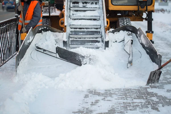 Trator limpando a estrada da neve. Escavadeira limpa as ruas de grandes quantidades de neve na cidade. Os trabalhadores varrem a neve da estrada no inverno, limpando a estrada da tempestade de neve — Fotografia de Stock