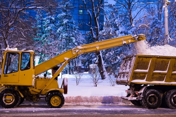 Pençe yükleyici araç karları yoldan çekiyor. Kar küreme aracı bir kamyona kar yağdırır. — Stok fotoğraf
