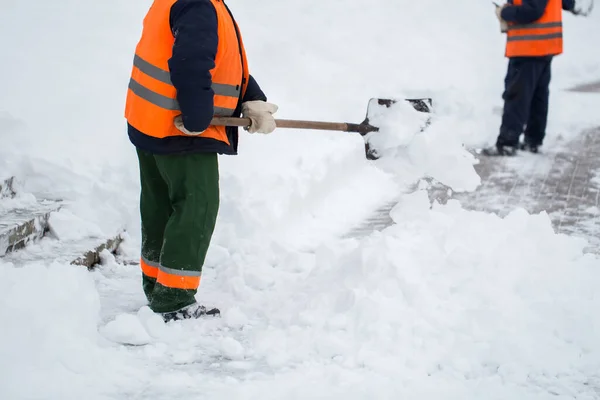 Employees of municipal services in a special form are clearing snow from the sidewalk with a shovel — Stock Photo, Image