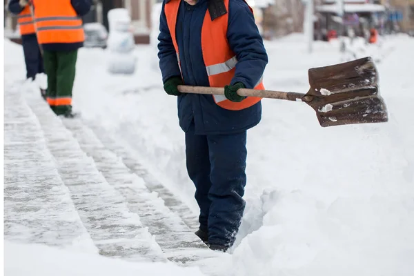 Funcionários de serviços municipais em uma forma especial estão limpando neve da calçada com uma pá — Fotografia de Stock