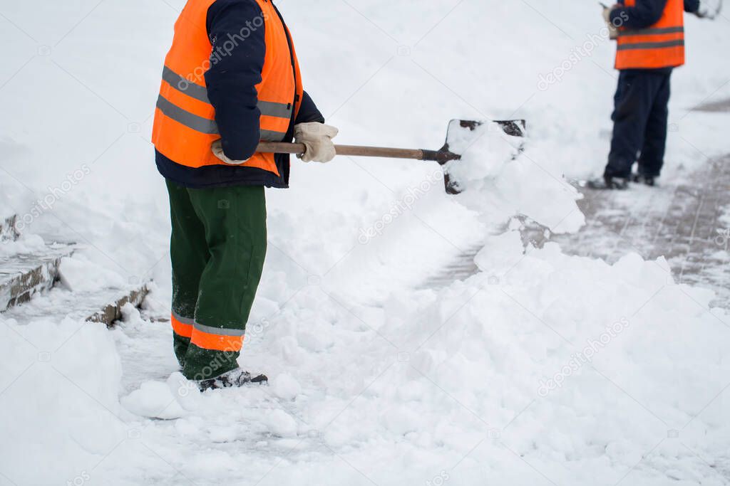 Employees of municipal services in a special form are clearing snow from the sidewalk with a shovel