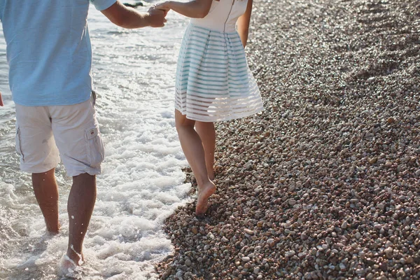 Pár kéz a kézben sétált a kavicsokon a tenger közelében. — Stock Fotó