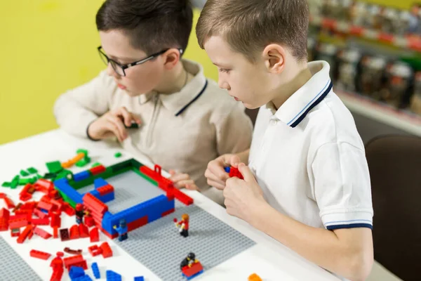 As crianças brincam no designer na mesa. Dois meninos jogam juntos com blocos de plástico coloridos no centro de jogos, escola — Fotografia de Stock