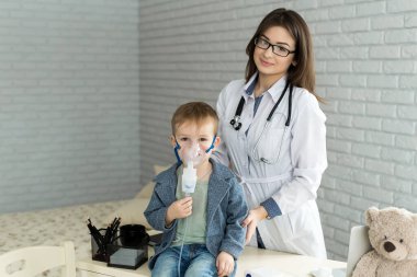 Tıp doktoru astım tedavisi gören küçük bir çocuğa solunum maskesi ile ilaç tedavisi uyguluyor.