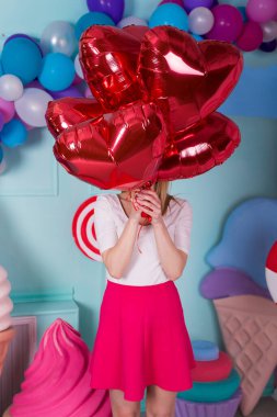 Pembe elbiseli, balonlu, renkli arka planda şekerlemeleri olan genç bir kadının moda portresi.
