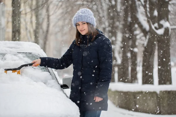 Uma mulher remove a neve do pára-brisas de um carro. — Fotografia de Stock