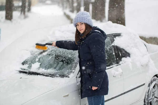 Uma mulher remove a neve do pára-brisas de um carro. — Fotografia de Stock