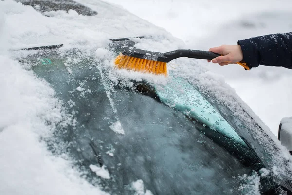 Uma mulher remove a neve do pára-brisas de um carro. — Fotografia de Stock