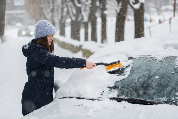 Uma mulher remove a neve do pára-brisas de um carro. — Fotografia de Stock