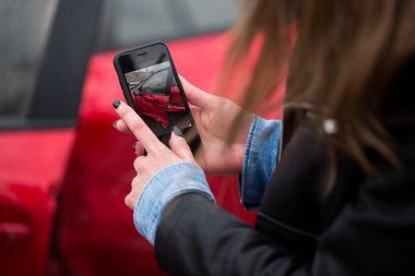 Araba kazasının yol açtığı hasarın fotoğrafını çekmek için akıllı telefon kullanan bir kadın..