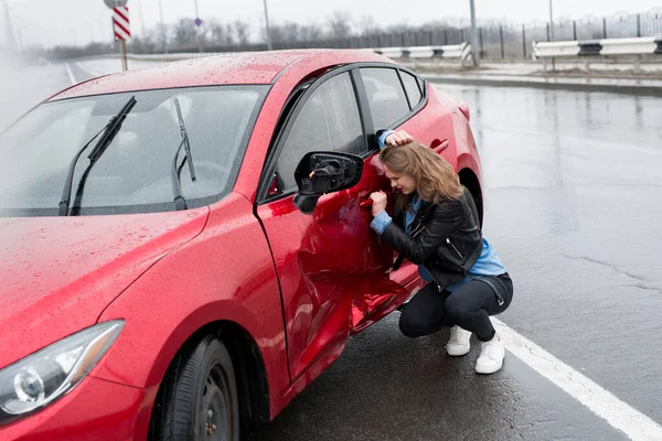 Mulher senta-se perto de um carro quebrado após um acidente. Pede ajuda. seguro automóvel . — Fotografia de Stock