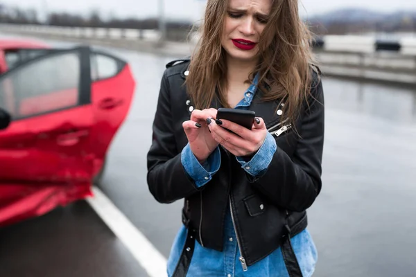 Mujer llama a un servicio de pie junto a un coche rojo . — Foto de Stock