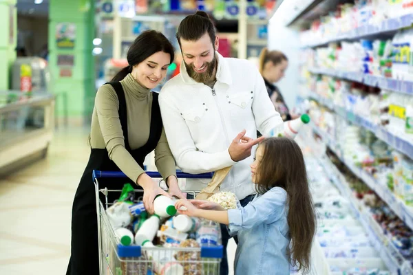 Молодая семья с ребенком выбирают молоко в супермаркете — стоковое фото