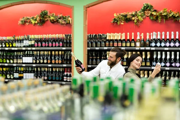 Egy fiatal család, egy férfi és egy nő az alkoholt választja egy nagy szupermarketben. — Stock Fotó
