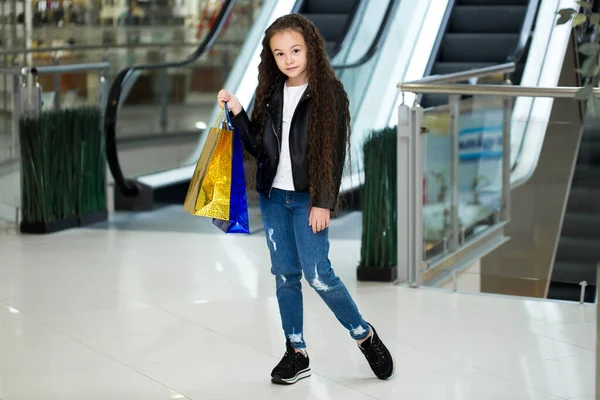 Het vrolijke kind met kleurenpakketten op de roltrap, in de winkel van winkelcentrum. — Stockfoto
