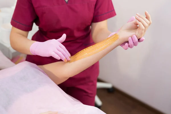 Sugaring. Beauty Concept. Young beautiful girl with dark hair gets the procedure for hair removal liquid sugar. Depilation and beauty concept - procedure of hair removing on hand on a beautiful woman. — Stock Photo, Image