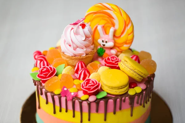 Barevný dort pro děti narozeninová oslava s lízátkem, sladkostmi, marmeládou, košíčky a králíčky. — Stock fotografie