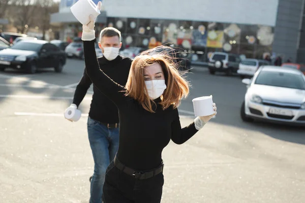 Donna e un uomo in maschera coronavirus tenere grandi rotoli di carta igienica su una strada della città e indulgere — Foto Stock