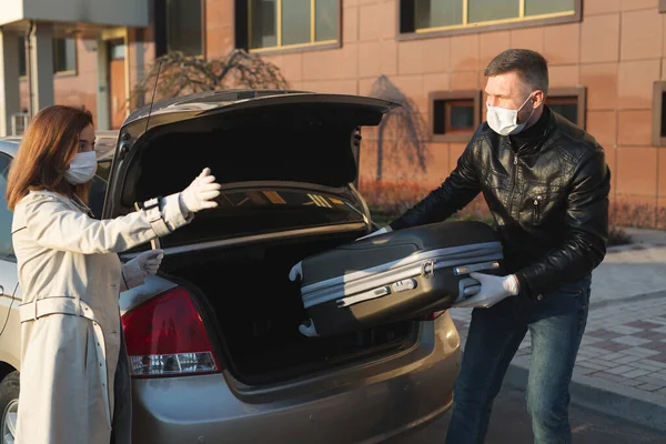 의료용 마스크와 장갑을 착용 한 한 남성 과 여성은 격리와 고립 기간 동안 트렁크에 가방을 싣고 차를 타고 집을 나왔다. 코로나 바이러스. covid 19 — 스톡 사진