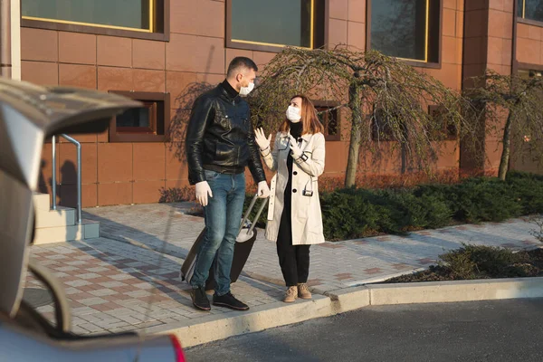 Hombre y mujer con máscaras y guantes médicos protectores con una maleta salen de la casa en coche durante la cuarentena y el autoaislamiento. El coronavirus. Covid 19 —  Fotos de Stock