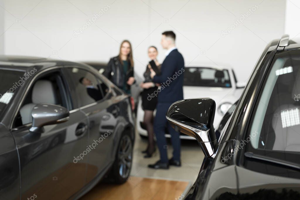 Auto business, car sales - a couple of friends of girls with a car dealer choose a car in a car dealership.