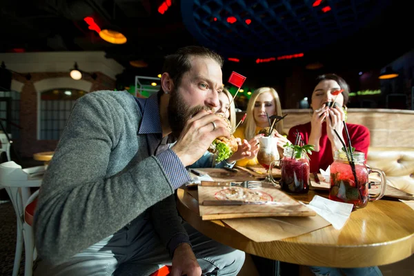 Az emberek együtt vacsoráznak egy kávézóban. A boldog barátok hamburgert esznek és jól érzik magukat. — Stock Fotó