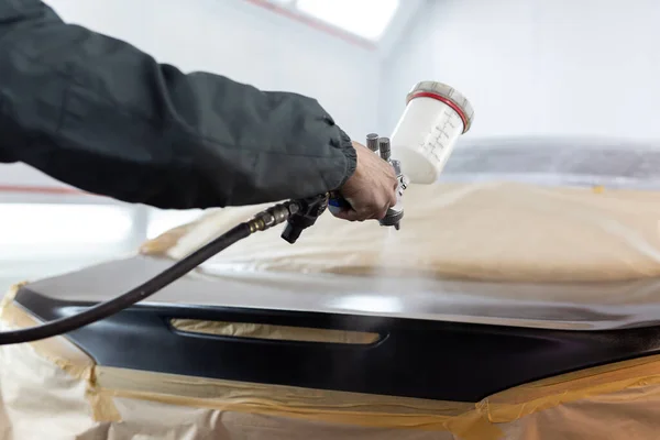 Primer plano de una pistola pulverizadora con pintura negra para pintar un coche en una cabina especial —  Fotos de Stock