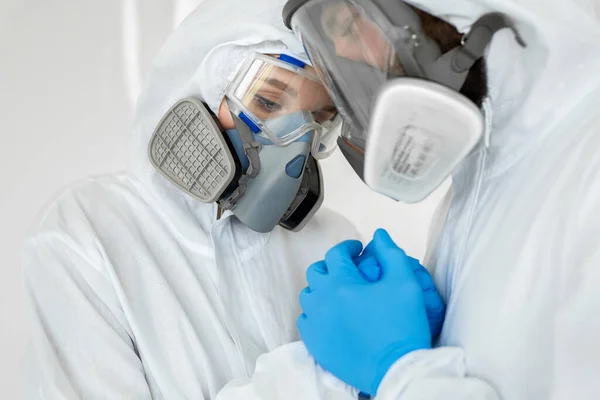 Portretten van de arts: een man en een vrouw in beschermende pakken en ademhalingstoestellen die elkaars hand vasthouden tijdens de quarantaine. Covid-19 — Stockfoto