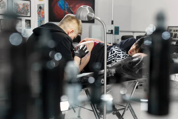 Tatuaggio artista professionista fa un tatuaggio su una gamba di giovani ragazze . — Foto Stock