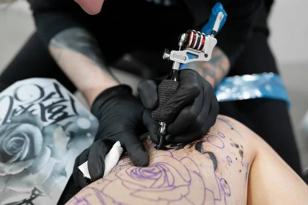 Close up image of the bearded tattoo male artist makes a tattoo on a female leg. — Stock Photo, Image