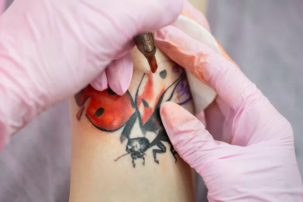 針タトゥーマシンは女の子の皮膚に赤いインクを注入します。皮膚に入れ墨を適用するプロセスのクローズアップ. — ストック写真