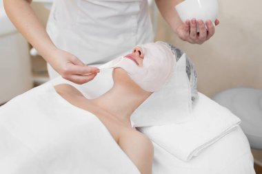 Yüz Peeling Maskesi, Spa Güzellik Bakımı, Cilt Bakımı. Spa Salon'da Güzellik Uzmanı ndan Yüz Bakımı Alan Kadın. Kadın Aljinat Maskesi Yapar. Bej Kil Maskeli Kız.