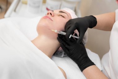 Kozmetik uzmanı genç bir kıza yaşlanma karşıtı iğneler yapıyor. Güzellik uzmanımız yüzdeki biyoevrizma prosedürünü uygular. Enjeksiyondan elde edilen kan ciltte görünür.