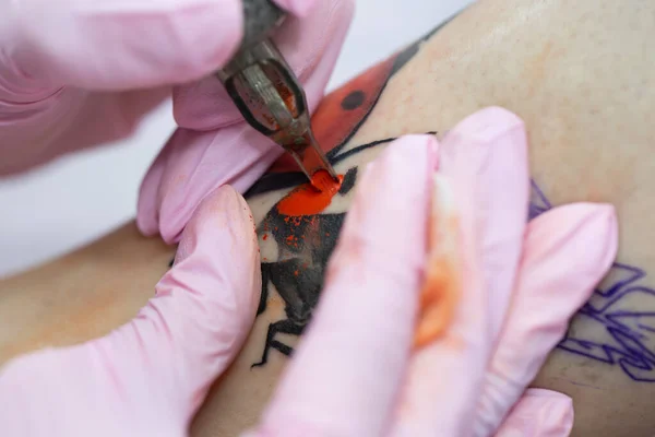 針タトゥーマシンは女の子の皮膚に赤いインクを注入します。皮膚に入れ墨を適用するプロセスのクローズアップ. — ストック写真