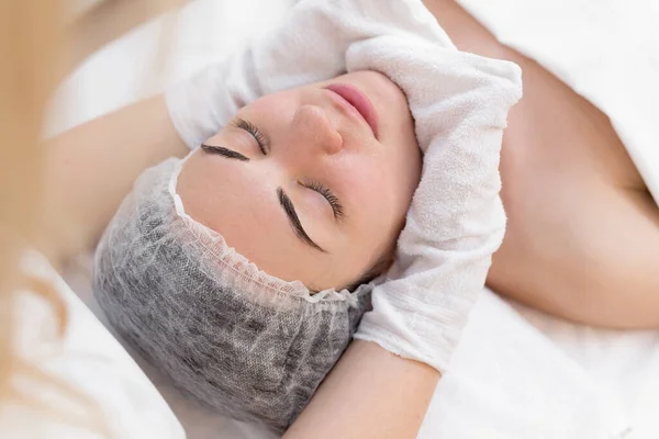 Les mains de l'esthéticienne essuient le visage des filles dans le centre de cosmétologie avec des gants blancs. Portrait d'une belle fille sur la procédure pour rajeunir le visage dans un salon de beauté. — Photo