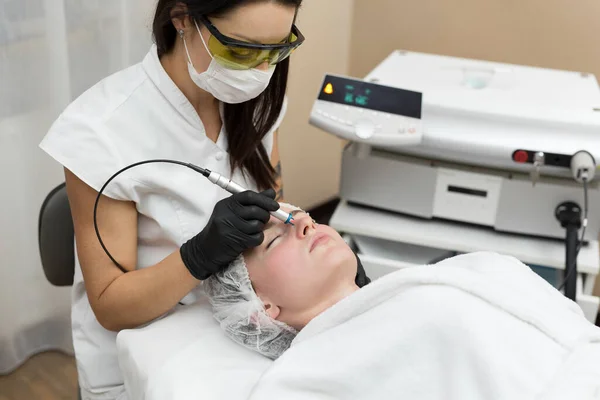 Kosmetolog w okularach ochronnych przeprowadza laserowe leczenie skóry dla młodego pacjenta w klinice kosmetologicznej. Usuwanie naczyń za pomocą lasera diodowego. — Zdjęcie stockowe