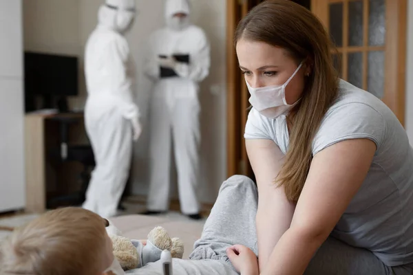 Mama misst die Temperatur der Babys. Ärzte in Schutzanzügen bei kranken Patienten zu Hause. Coronavirus, Covid-19 — Stockfoto
