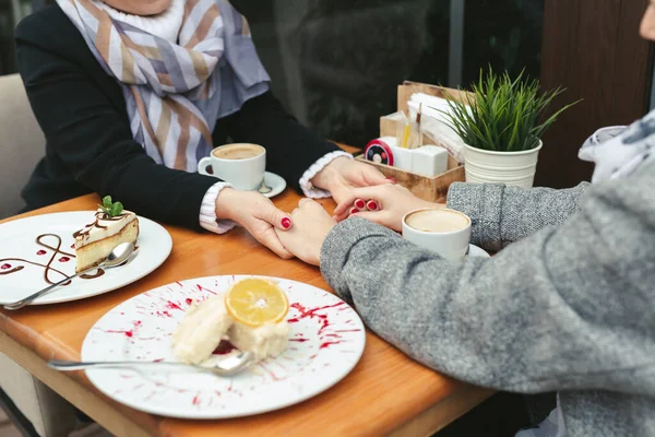 Close-up van een moeder en dochters handen op een houten tafel in een café. Volwassen moeder en dochter houden elkaars hand vast en drinken koffie — Stockfoto