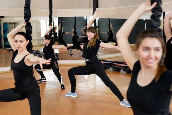 Groep actieve sportmeisjes in zwarte sportkleding houden zich bezig met budgie fitness in de sportschool. Bungeejumpen in de sportschool. — Stockfoto